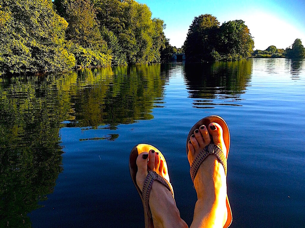 Nackte Fueße baumeln ueber einem leuchtend blauen Fluss 